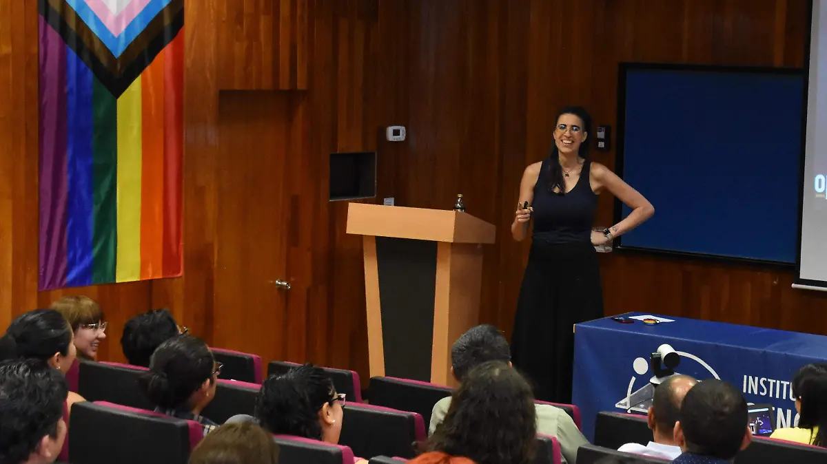 Ophelia Pastrana dando una charla junto a la bandera del orgullo progresista.