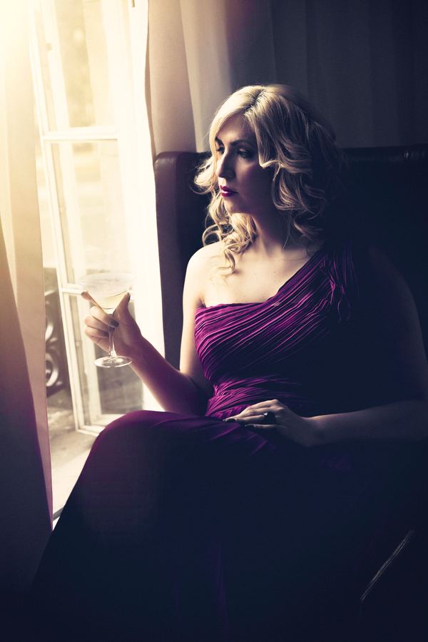 Ophelia con vestido morado largo junto a una ventana, luz tenue.