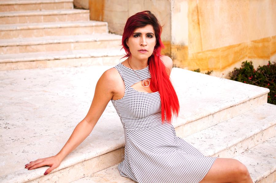 Ophelia sentada en unos escalones con vestido gris y pelo rojo. Horizontal.