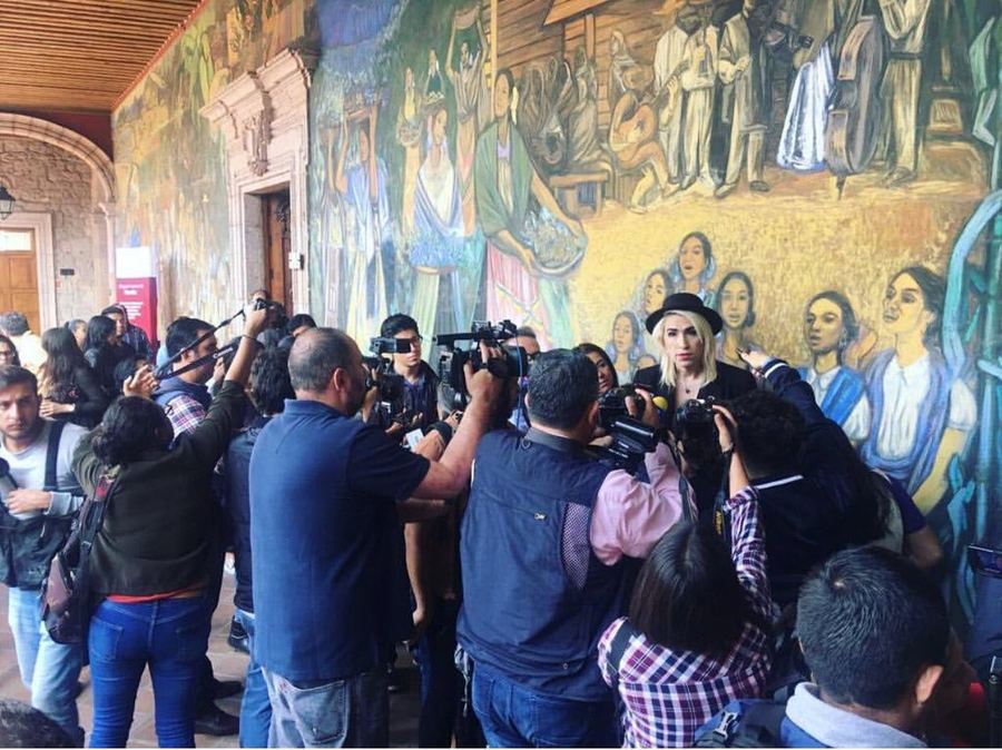 Rueda de prensa frente a un mural, con cámaras y micrófonos. Horizontal.