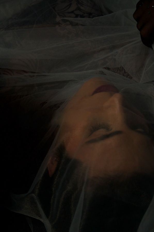 Ophelia bajo un plástico translúcido, fondo oscuro. Vertical.