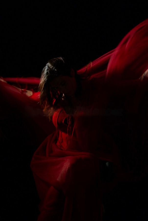 Ophelia envuelta en tela roja en movimiento, fondo oscuro. Vertical.