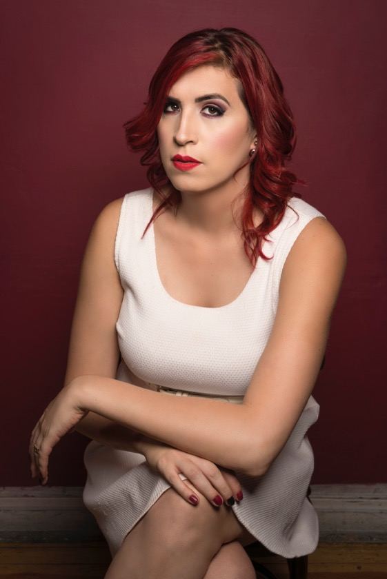 Ophelia con pelo rojo y vestido blanco, sentada frente a una pared vino.