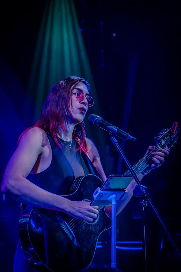 Ophelia cantando con guitarra bajo luz azul en Lenchafest 2025. Vertical.