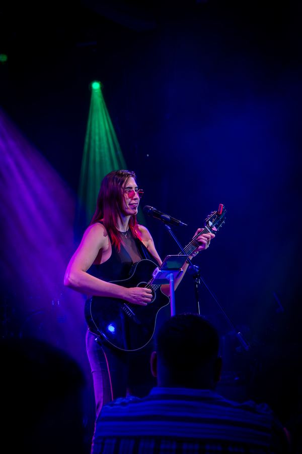 Ophelia con guitarra bajo luz morada y azul en Lenchafest 2025. Vertical.