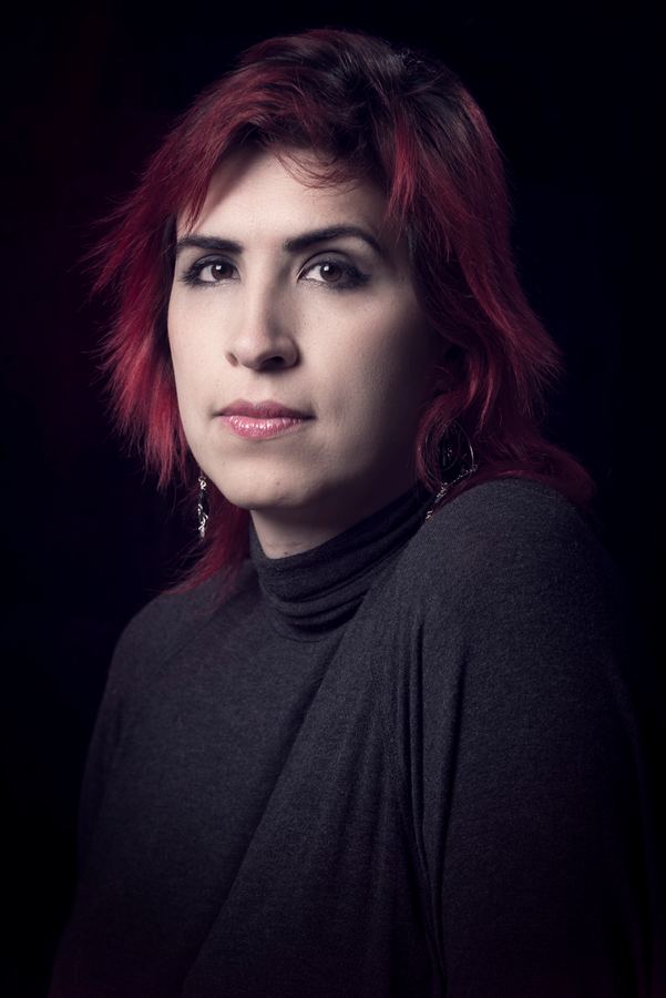 Ophelia con pelo rojo mirando a cámara, fondo negro. Vertical.