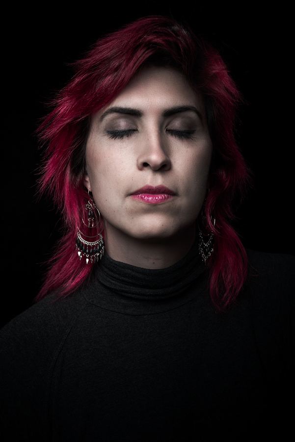 Ophelia con pelo rojo y ojos cerrados, fondo negro. Vertical.