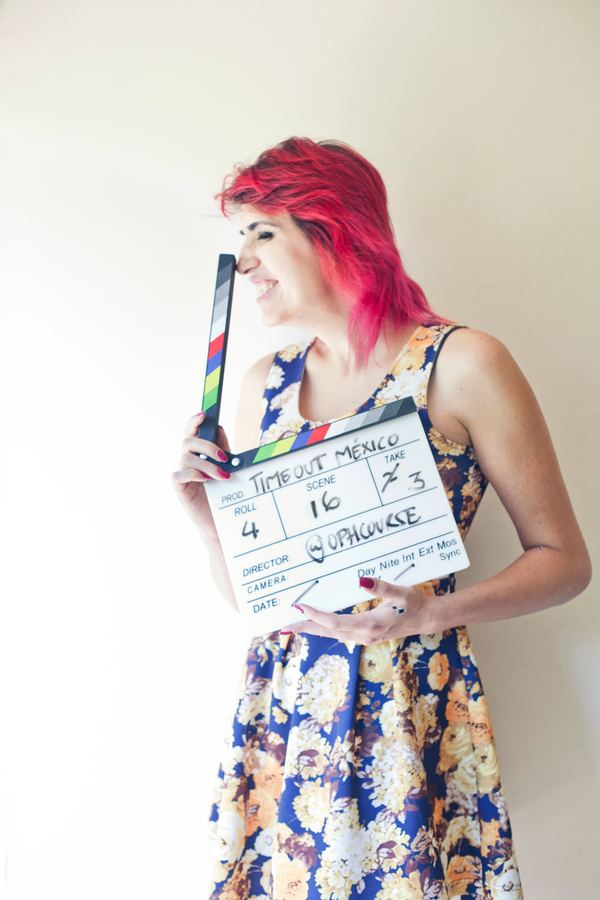 Ophelia con una claqueta de cine, sonriendo, pared blanca.