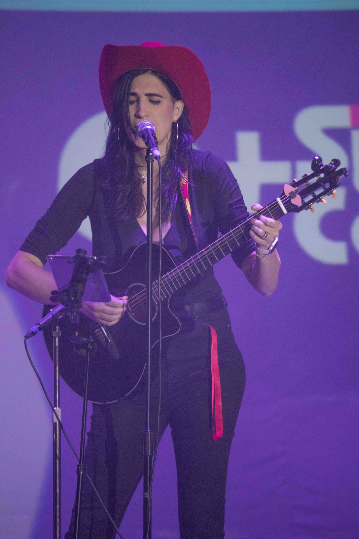 Ophelia tocando la guitarra con sombrero vaquero, escenario morado. Vertical.