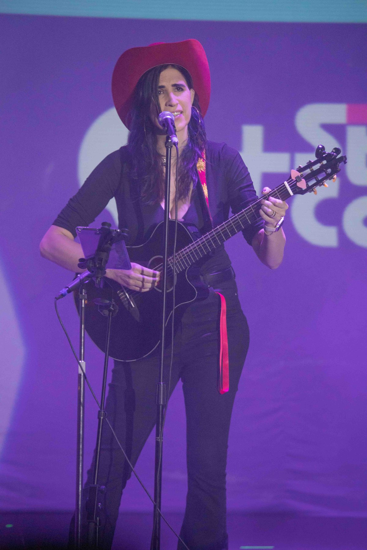 Ophelia cantando con guitarra y sombrero vaquero, escenario morado. Vertical.