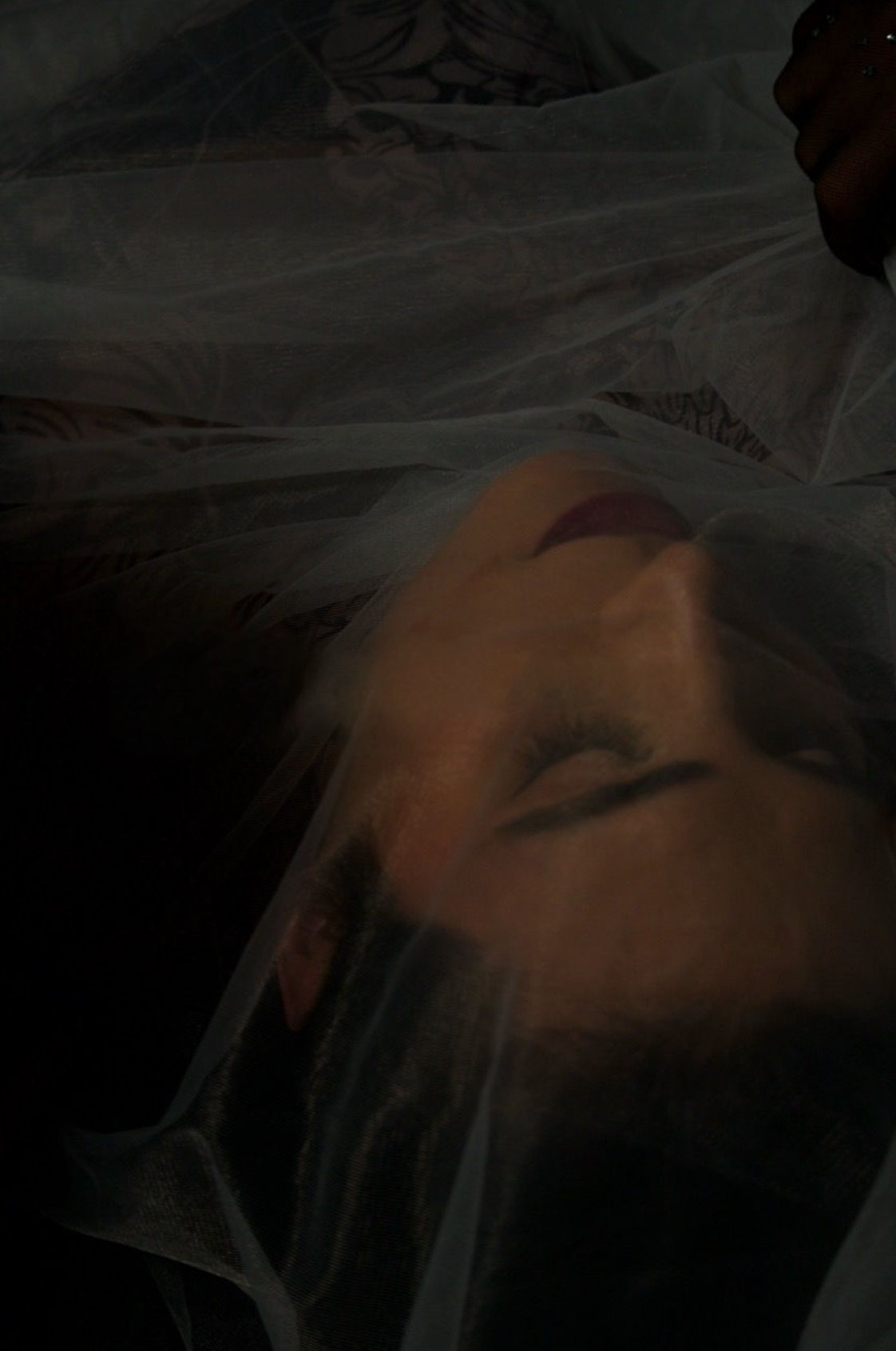 Ophelia bajo un plástico translúcido, fondo oscuro. Vertical.