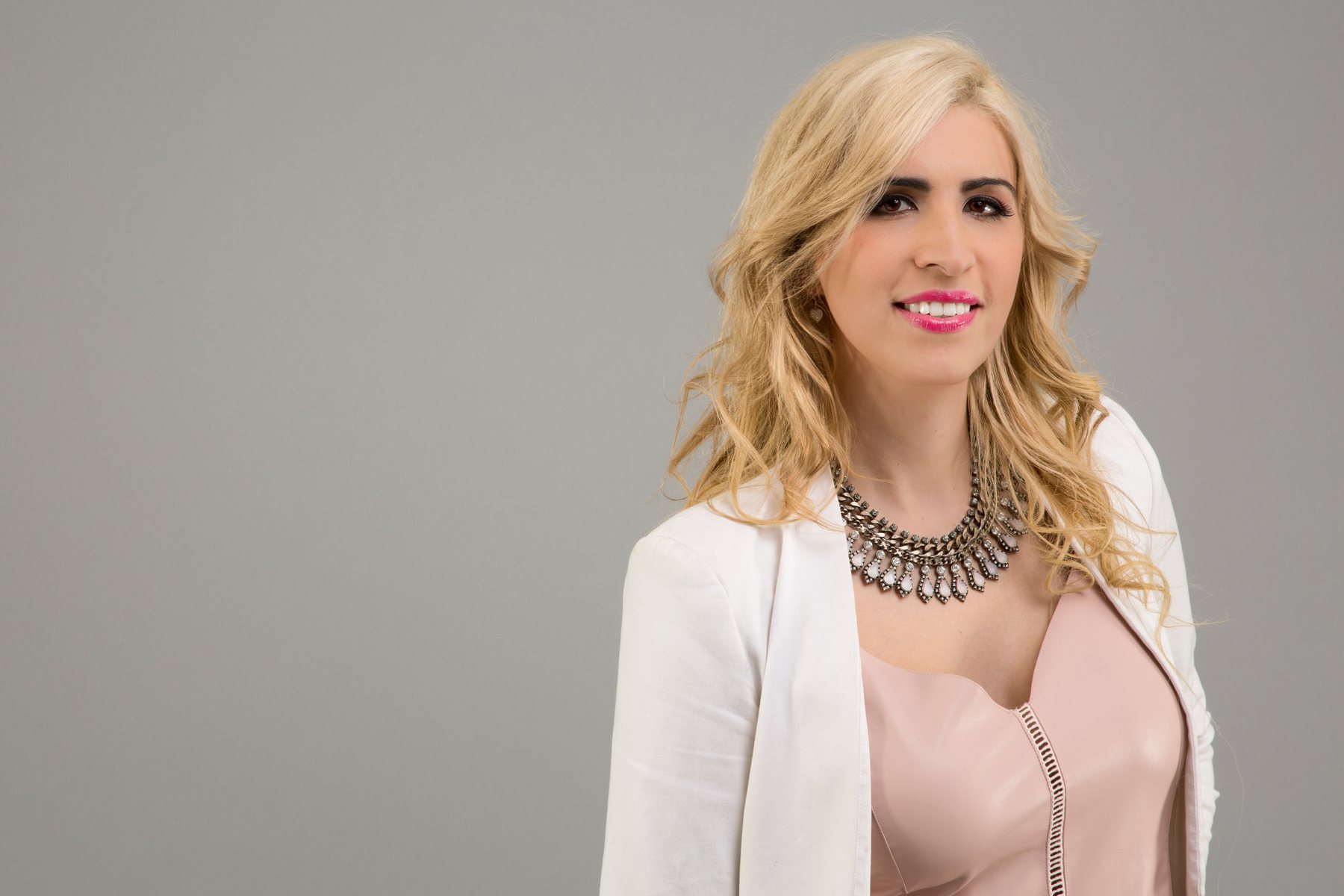 Ophelia con saco blanco y collar, sonriendo, fondo gris. Horizontal.