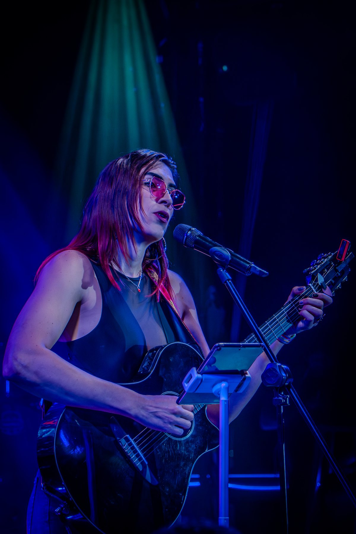 Ophelia cantando con guitarra bajo luz azul en Lenchafest 2025. Vertical.