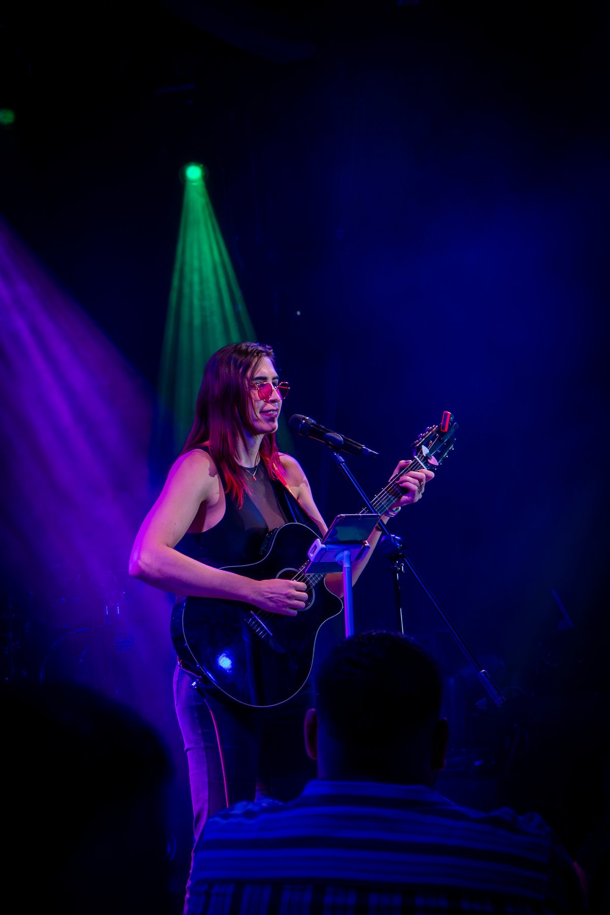 Ophelia con guitarra bajo luz morada y azul en Lenchafest 2025. Vertical.