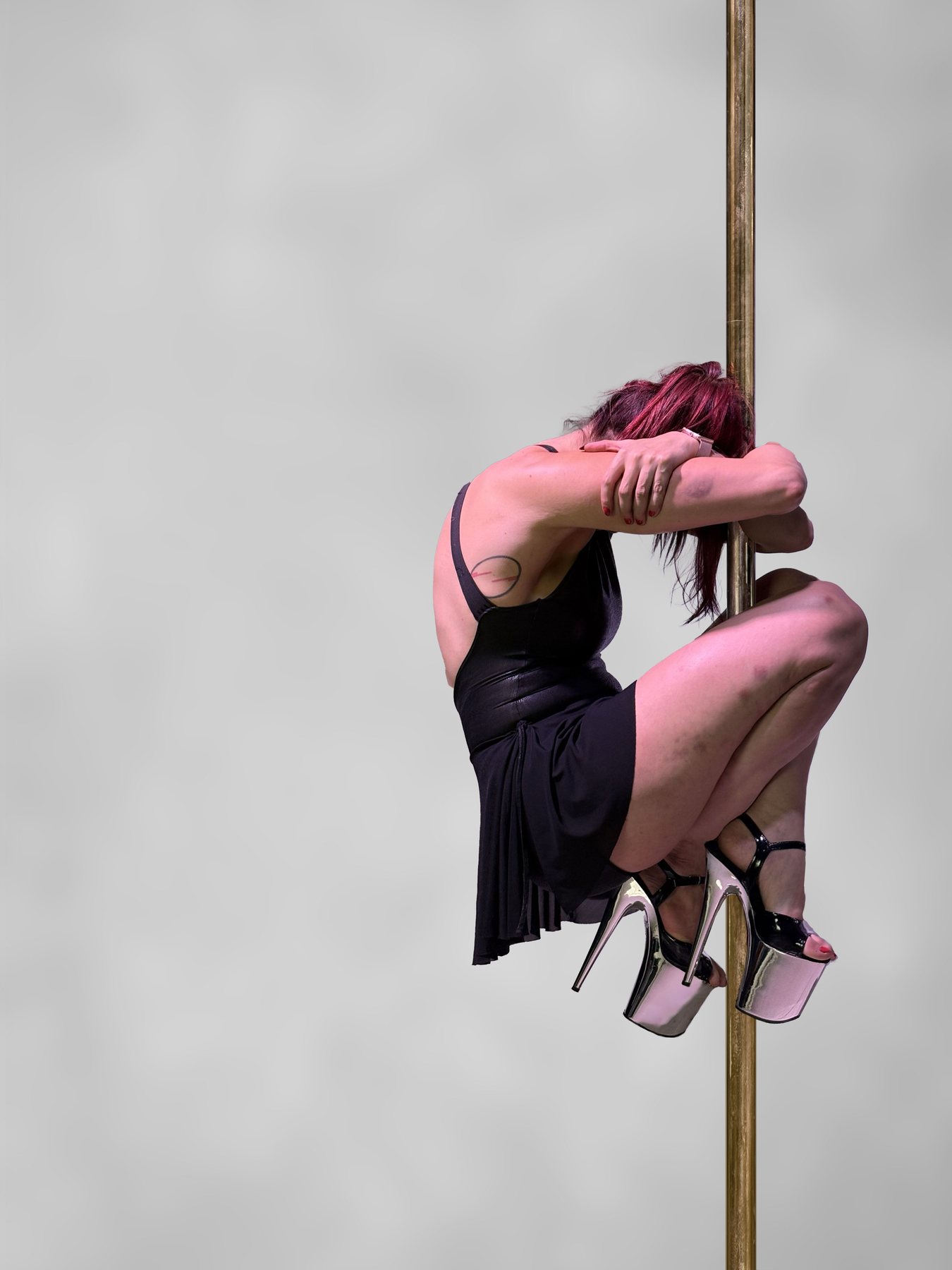Ophelia abrazada al tubo de pole con vestido rosa, fondo claro al aire libre. Vertical.